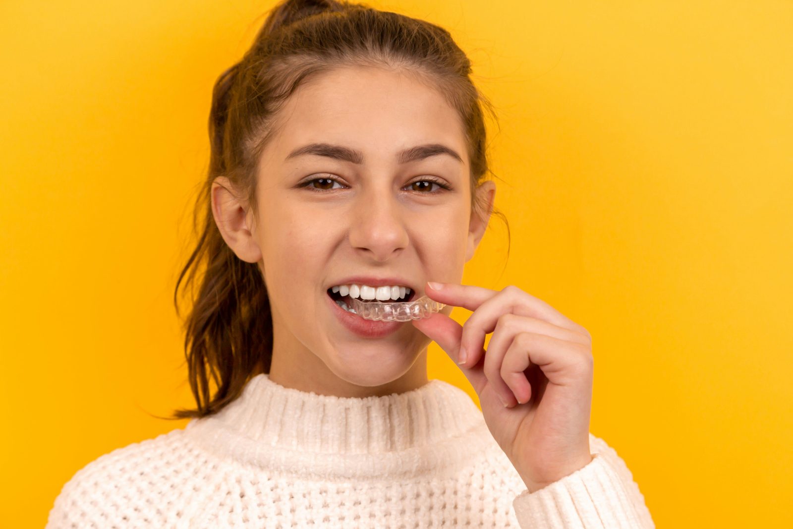 A person holding a clear aligner tray and smiling in a bright dental clinic